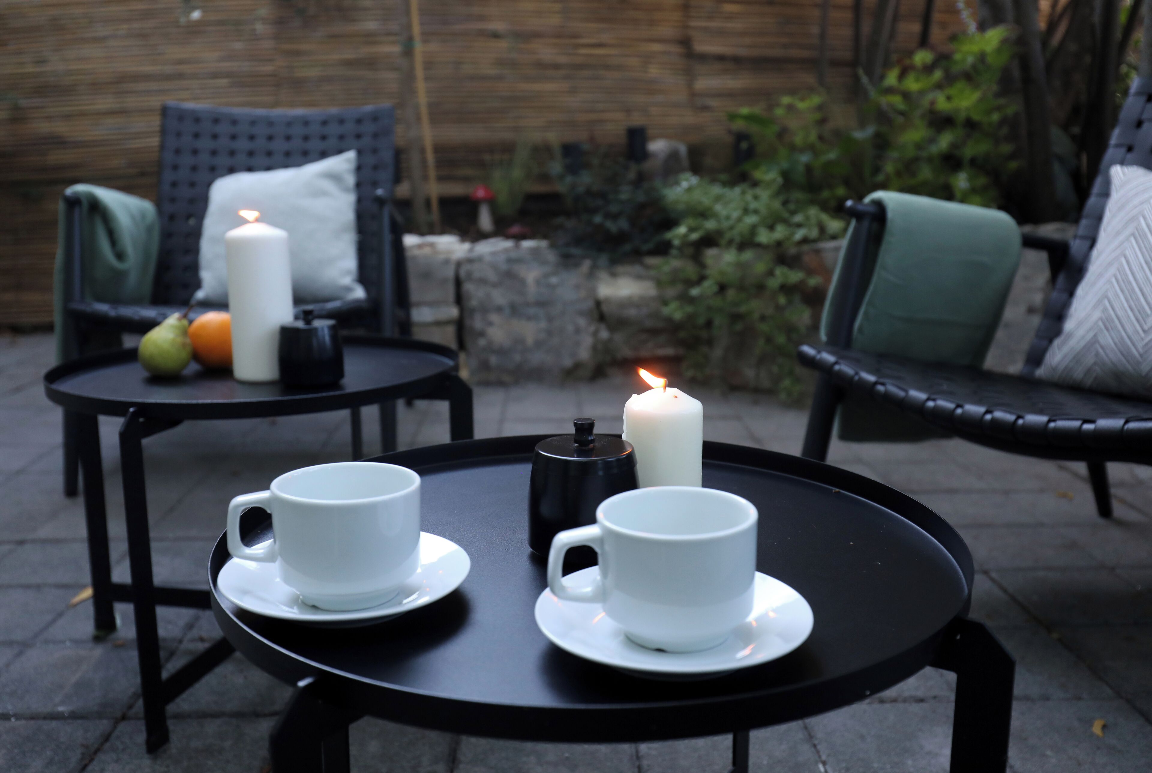 Two round tables with white cups and saucers, a candle, and a small black container.