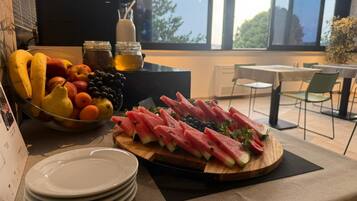 Un tavolo con una ciotola di frutta, un tagliere con fette di anguria e una pila di piatti bianchi.