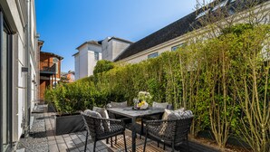 A patio with a table and chairs, surrounded by a hedge and buildings. - Luxury duplex apartment with terrace (Sylt)