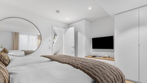 A modern hotel room with a large bed, a round mirror, a flat-screen TV, and a wardrobe. - Luxury duplex apartment with terrace (Sylt)