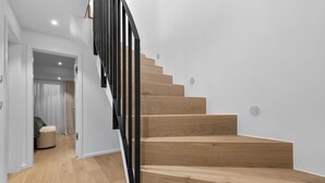 A modern staircase with wooden steps and black railings, leading to a room with a light-colored floor and a door. - Luxury duplex apartment with terrace (Sylt)