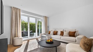 A modern living room with a sofa, coffee table, and a view of greenery through large glass doors. - Luxury duplex apartment with terrace (Sylt)