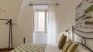 A bedroom with a bed, a hanging light, a painting on the wall, and a window with curtains.