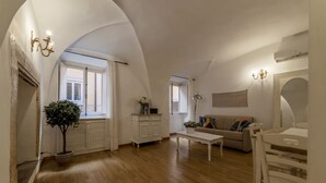 A spacious living room with wooden flooring, a white sofa, a coffee table, and a dining area with white chairs.