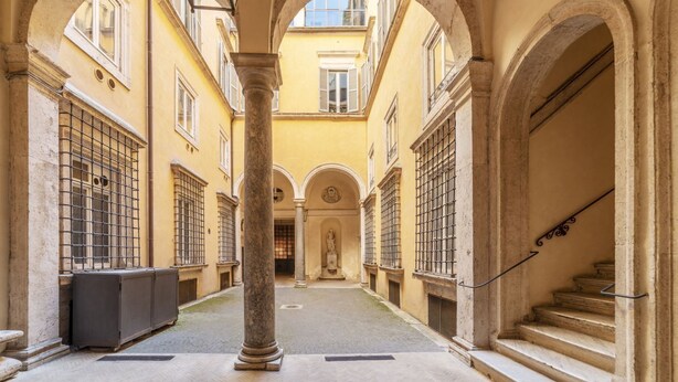 A narrow corridor with arches, a statue, and a staircase.