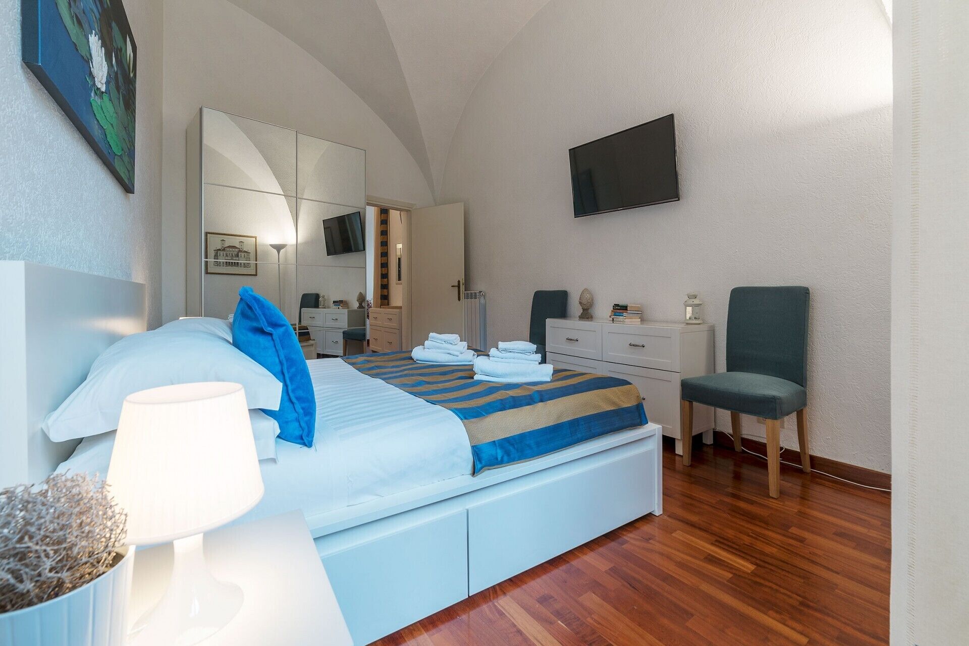 A hotel room with a large bed, a desk, a chair, a TV, and a mirror.