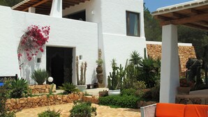 A modern white building with a stone facade, a wooden pergola, and a variety of plants and cacti in the garden. - My Rental Homes - Villa Sun with sea view, pool and large garden (Sant Antoni De Portmany)