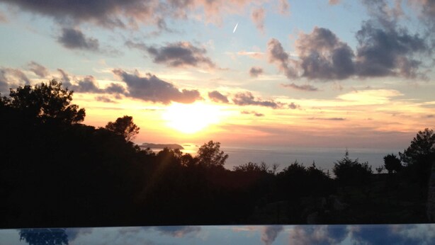 A sunset over a body of water with trees silhouetted against the sky. - My Rental Homes - Villa Sun with sea view, pool and large garden (Sant Antoni De Portmany)
