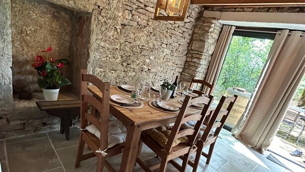A rustic dining area with a stone wall, wooden table, and chairs. - Gîte "la Cazelle (Saint-Chels)