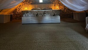 A cozy attic bedroom with a stone wall, a bed with floral bedding, and sheer drapes. - Gîte "la Cazelle (Saint-Chels)