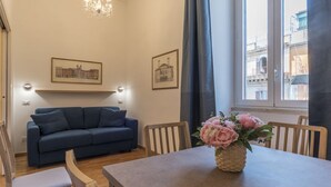 A cozy living room with a blue sofa, wooden chairs, a dining table with a vase of flowers, and two framed pictures on the wall. - CS Termini Nazionale Apt n. 4 (Roma)
