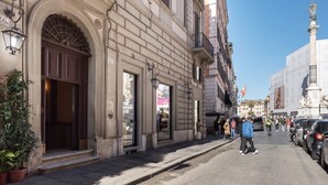 Une rue bordée d’un immeuble doté d’une grande entrée en arc de cercle, d’un magasin avec une enseigne bien visible et d’une statue située sur le côté droit.