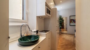 Une cuisine de taille réduite avec un évier vert, des placards blancs et une petite fenêtre.