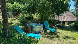A garden with a metal hot tub, two blue lounge chairs, and a stone structure in the background. - Gîte "Le Causse (Saint-Chels)