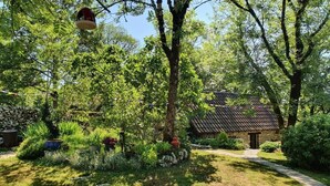 A garden with a stone house, a pathway, and a hanging bird feeder. - Gîte "Le Causse (Saint-Chels)