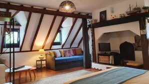 A cozy room with a sloped ceiling, a sofa, a television, and a bookshelf. - Gîte "Le Causse (Saint-Chels)