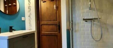 Un baño con puerta de madera, un lavabo blanco, un espejo y una zona de ducha.