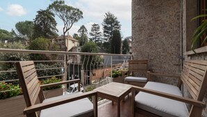 A balcony with wooden furniture, including two chairs and a small table, overlooking a residential area with trees and buildings. - CS Vatican Metro Apartment (Roma)