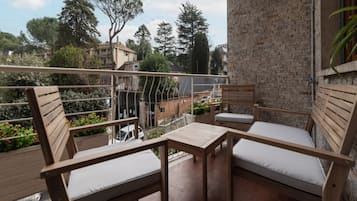 Un balcone con arredi in legno, tra cui due sedie e un tavolino, con vista su una zona residenziale con alberi e palazzi.