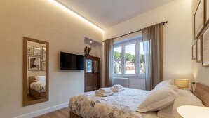 A bedroom with a bed, a flat-screen TV, a mirror, a window with curtains, and a radiator. - CS Vatican Metro Apartment (Roma)