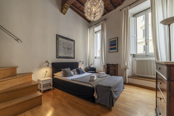 A bedroom with a bed, a nightstand, a dresser, a window with curtains, a radiator, and a staircase. - CS Navona / Castel S. Angelo Apartment (Roma)