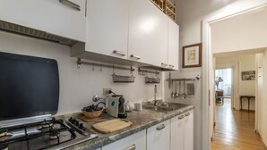 Een moderne keuken met witte kastjes, een gasfornuis en een aanrecht met diverse apparaten en keukengerei.
