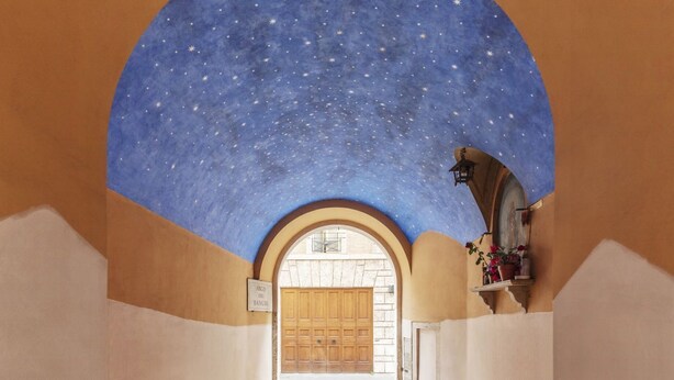 Een gang met een sterrenhemelplafond, een houten deur en een bordje met de tekst 'ARCO DE BANCHE'.