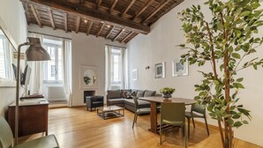 Een ruime woonkamer met een houten plafond, een bank, een eettafel en een potplant.