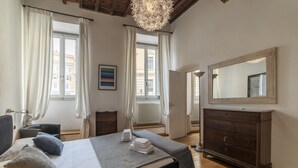 Een slaapkamer met een bed, nachtkastjes, een dressoir, een grote spiegel en een raam met gordijnen.