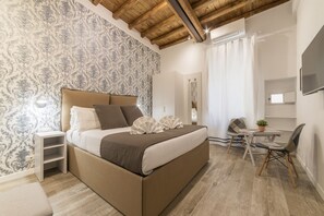 Une chambre avec un grand lit, une table de chevet, une chaise, une petite table avec une plante et un miroir au mur.