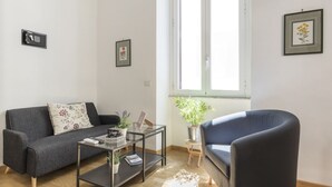 A living room with a grey sofa, a black armchair, a glass coffee table, and a small side table with a plant.