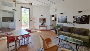 A spacious living area with a dining table, sofa, and chairs, a kitchen in the background, and a large window providing natural light. - CS Stylish Loft with Terrace (Roma)