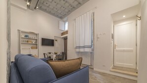 A modern living room with a blue sofa, a dining table with chairs, a TV mounted on the wall, and a white door. - CS Exclusive Campo de' Fiori Palace apt. 2 (Roma)