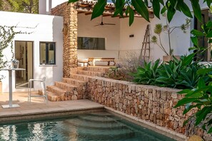 A pool area with stone steps leading to a covered seating area, surrounded by lush greenery. - Can Blanca with pool - My Rental Homes (Sant Antoni De Portmany)
