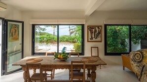 Ein Essbereich mit Tisch, Stühlen und einer Schüssel mit Obst. Große Fenster bieten Blick auf grüne Natur.