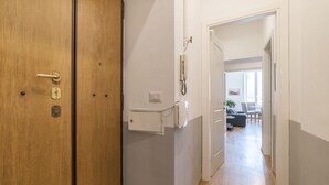 A hallway with a wooden door, a white wall, a telephone, and a glimpse of a living area with a sofa and a table. - CS Central Station Termini / Monti Apartment (Roma)