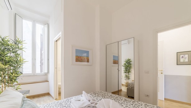 A modern hotel room with a large bed, a mirror, a potted plant, and a window with a view of buildings. - CS Central Station Termini / Monti Apartment (Roma)