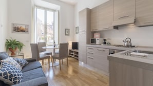 A modern kitchen with wooden cabinets, a microwave, kettle, and a dining area with a table and chairs. - CS Central Station Termini / Monti Apartment (Roma)