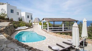 A pool area with stone tiles, lounge chairs, and a pergola with a thatched roof overlooking a mountainous landscape. - My Rental Homes - Villa Rigel with private pool and terraces (San Jose)