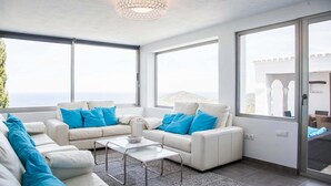 A modern living room with two white sofas, a glass coffee table, and large windows offering a view of the sea. - My Rental Homes - Villa Rigel with private pool and terraces (San Jose)