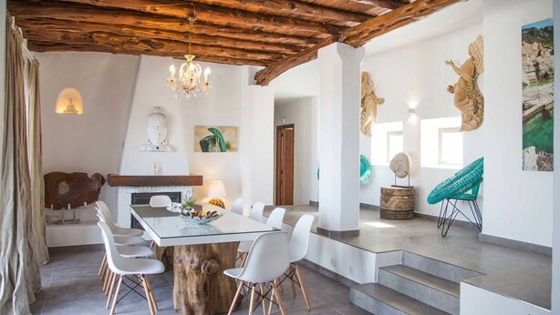 A modern dining area with a wooden table and chairs, a chandelier, and artwork on the walls. - My Rental Homes - Villa Rigel with private pool and terraces (San Jose)
