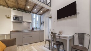 Een moderne keuken met een ingebouwde magnetron, een eethoek met twee stoelen, en een aan de muur bevestigde televisie.