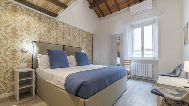 Een slaapkamer met een groot bed, nachtkastje, stoel en een raam met uitzicht.
