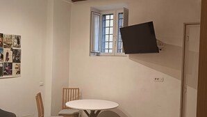 A small, compact room with a bed, a round table, a chair, and a TV mounted on the wall.