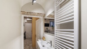 A narrow hallway leading to a bathroom with a white sink and a towel rack.