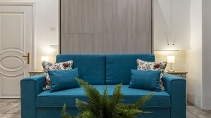 A blue sofa with floral cushions, two bedside lamps, and a green plant in front.