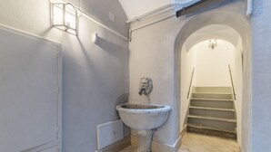 A bathroom with a large, rustic sink, a wall-mounted light fixture, and a staircase leading to another level.