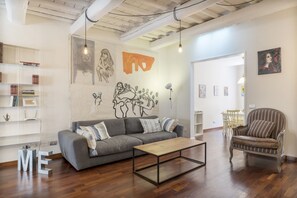 A modern living room with a grey sofa, a wooden coffee table, and a striped armchair. There are bookshelves and artwork on the walls. - Industrial Chic Loft Apartment in Historical Building (Roma)