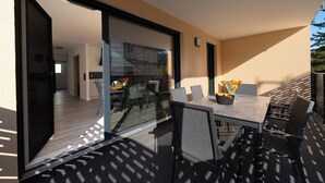 Et moderne udendørs spiseområde med glasvæg, et bord med stole og en blomsterdekoration.