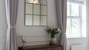 A room with a wooden console table, a mirror, a vase with flowers, and a window with curtains.